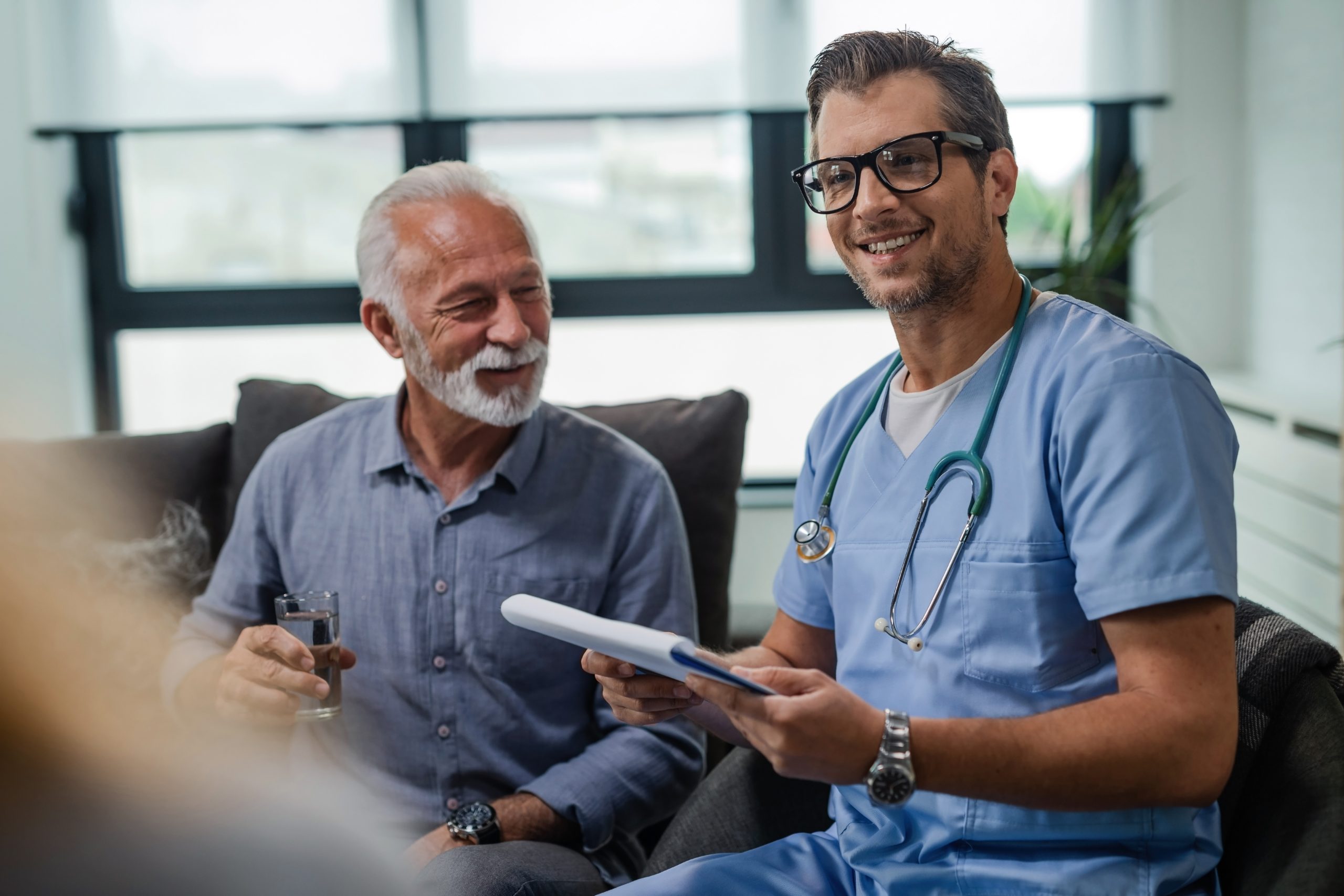 Happy mid adult healthcare worker in a home visit. Happy male doctor visiting senior patients at home and going through medical documents.