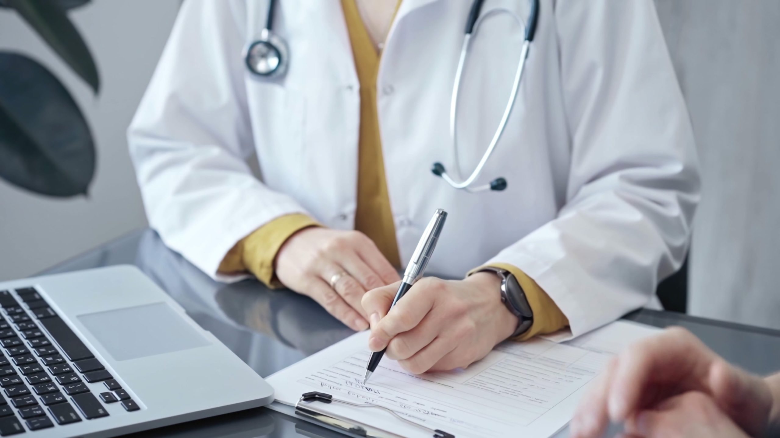Doctor completing paperwork with patient. Close-up of a doctor's hands with forms, imparting information to a laptop. Medicine and health care concept Doctor completing paperwork with patient. Close-up of a doctor's hands with forms, imparting information to a laptop. Medicine and health care concept.